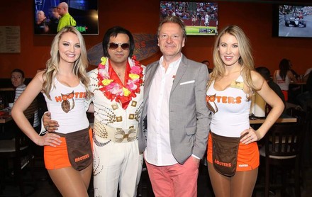 Zwei weibliche Servicekräfte der neuen Hooters-Filiale auf der Reeperbahn stehen neben zwei Männern von denen einer als Elvis verkleidet ist