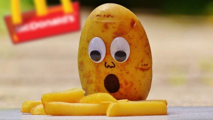 Eine Kartoffel mit Glupschaugen und einem offenen Mund blickt erstaunt auf ein paar Pommes