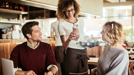Kellnerin mit Locken serviert Gästen im Restaurant einen Eiscafe