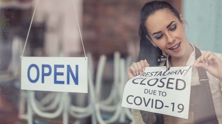 Junge Gastronomin entfernt ein Scild auf dem „Geschlossen wegen Covid-19 steht“
