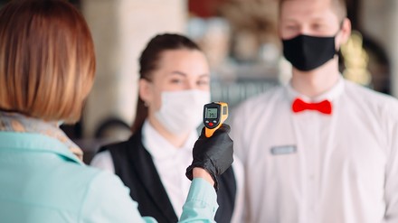 Personal mit Mundschutz, Chefin misst Fieber