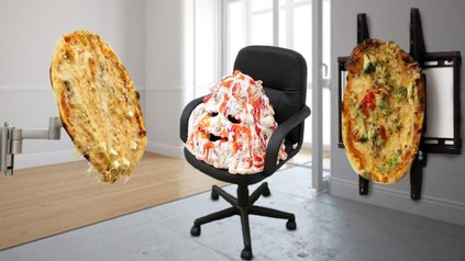 In einem Raum hängt eine Pizza an einer Fernsehhalterung, eine Pizza ist auf einem Bürostuhl platziert und scheint ein Gesicht zu haben, eine weitere Pizza ist an einer Bildschirmhalterung befestigt