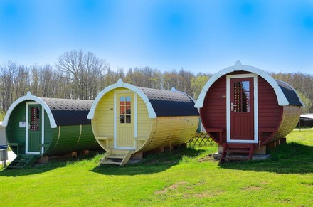 Drei bunte große Fässer in denen sich Hotelzimmer befinden auf einer Wiese