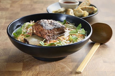 Vor allem die typisch japanischen, gehaltvollen Ramen-Suppen findet man im Wagamama in einer großen Auswahl. (© Wagamama)
Eine Schüssel Ramen auf einem Holztisch mit einem Holzlöffel