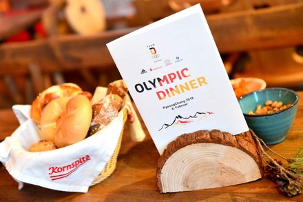 Ein gedeckter Frühstückstisch auf dem eine Proschüre platziert ist auf der Olympic Dinner steht