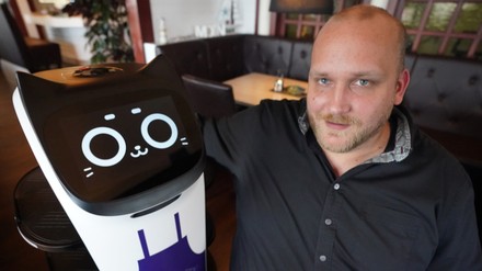 Gastwirt Tim Bornewasser sitzt in seinem Restaurant Hafenrestaurant neben dem Servierroboter „Bella“.