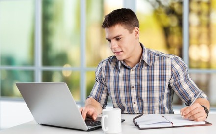 Mann arbeitet an Laptop mit Kaffee