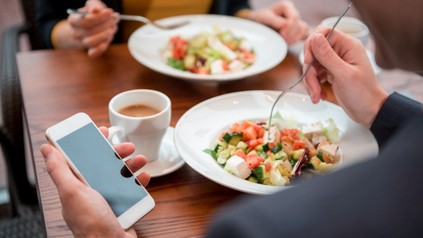 Mann isst in einem LOkal einen salat und schaut dabei auf sein Handy