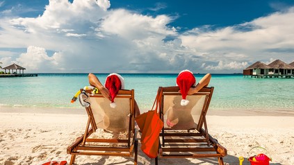 Zwei Urlauber sonenn sich mit Weihntachsmützen auf dem Kopf am Strand.