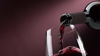 Rotwein wird vor lila Hintergrund in Weinglas geschenkt
