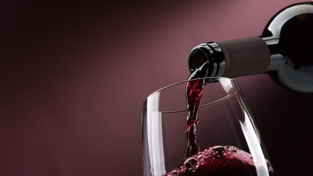 Edelsüße Weine werden als Beerenauslese oder Trockenbeerenauslese angeboten. (Foto: © stokkete – stock.adobe.com)
Rotwein wird vor lila Hintergrund in Weinglas geschenkt