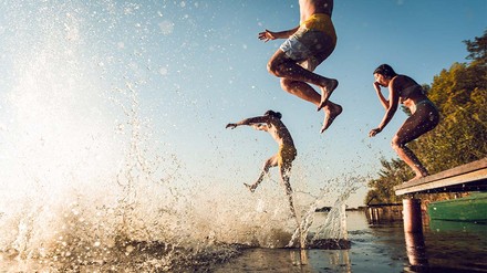 Junge Leute springen mit Anlauf vom Steg in den See