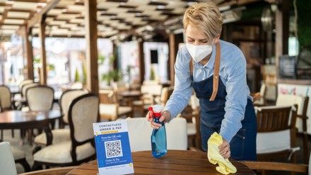 Mitarbeiterin mit FFP2 Maske reinigt Tisch