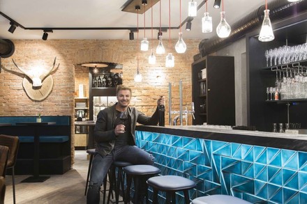 Leo Hillinger am Tresen mit Weinglas und Weinflasche in der Hand