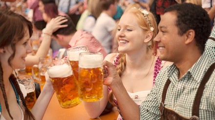 Junge Leute stoßen mit ihren Maßkrügen im Bierzelt auf der Wiesn an.