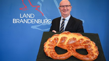 Brandenburgs Ministerpräsident Dietmar Woidke (SPD) erhält symbolisch für die Anstecknadel «Goldene Brezel» eine grosse Brezel aus gebackenem Teig. Die «Goldene Brezel» ist das Qualitätssiegel des Bäcker- und Konditorenhandwerks. Woidke erhielt die Auszeichnung für seine politischen Verdienste um das Handwerk in Brandenburg. (Foto: © picture alliance/dpa | Soeren Stache) Dietmar Woidke von Landesverband der Bäcker und Konditoren geehrt.