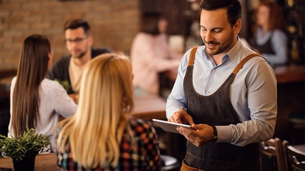 Oft werden mittlerweile Bestellungen im Restaurant über ein digitales Bestellsystem aufgenommen. (Foto: © Drazen/stock.adobe.com) Kellner nimmt Bestellung auf
