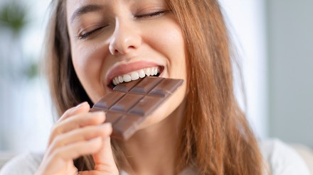 Wie schmeckt kakaofreie Schokolade? (Foto: ©dragonstock/stock.adobe.com) Eine Frau beißt genüsslich in eine Tafel Schokolade.
