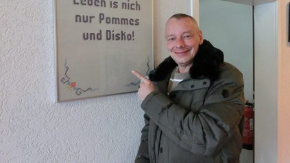 Harry Schulz zeigt auf Tafel mit Inschrift: "Leben ist nich nur Pommes und Disko!"