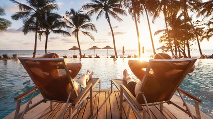 Reisende stocken für den Sommerurlaub ihre Budgets auf. (Foto: © Song_about_summer/stock.adobe.com) Zwei Urlauber liegen auf Liegestühlen an einem Pool