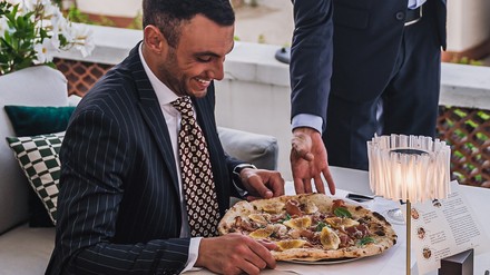 Gäste dürfen sich in dieser Saison auf die schmackhaften Pizzen der L´Antica Pizzeria da Michele freuen . (Foto: © Hotel Excelsior Venice Lido Resort) Ein Mann in Anzug bekommt eine Pizza serviert.