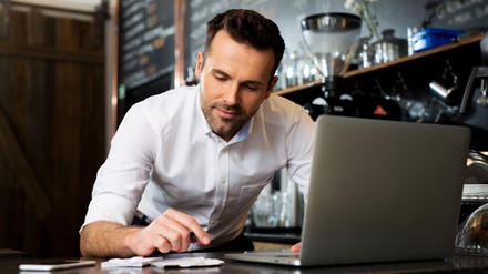 Die Schlussabrechnung kann jetzt noch bis zum 31. August eingereicht werden. (Foto: © baranq/stock.adobe.com) Gastronom bearbeitet etwas vor einem Computer