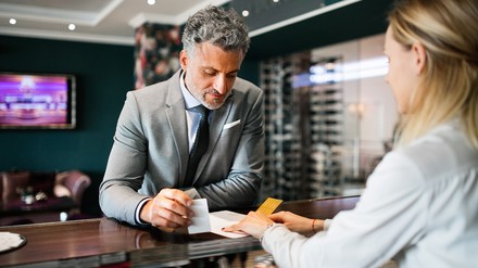 Ein Anreiz für Geschäftsreisen sind für Mitarbeiter auch Treueprogramme. (Foto: © Halfpoint/stock.adobe.com) Geschäftsreisender an der Rezeption