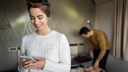 Der Chatbot Cubby ist der neue Reisebegleiter für Gäste von The Ascott Limited. (Foto: © Miljan Živković/stock.adobe.com) Frau schaut in einem Hotelzimmer auf ihr Handy.