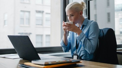Frau sitzt am Laptop und trinkt aus einer Tasse