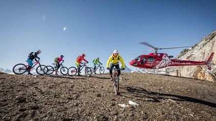 Eine Gruppe Radfahrer auf einem Berg und im Hintergrund ein roter Helikopter