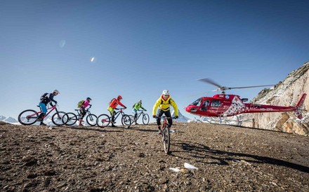 Eine Gruppe Radfahrer auf einem Berg und im Hintergrund ein roter Helikopter