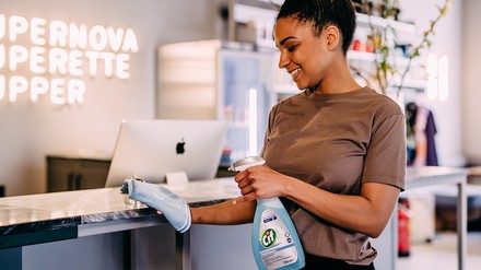 Lächelnde Frau sprüht Reinigungsmittel der Marke Cif auf ein Tuch