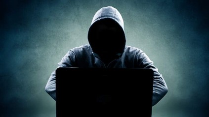 Eine Person mit dunkler Kapuze sitzt vor einem Laptop