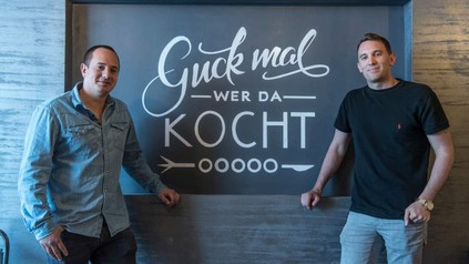 Hernando Ospina und Daniele Marino stehen vor einem Schild auf dem Guck mal wer da kocht steht