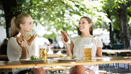 Zwei hübsche Frauen sitzen in einem Biergarten und essen eine Riesenbreze