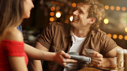 Junger Mann bezahlt bargeldlos in einem Restaurant, lächelnd, gute Stimmung