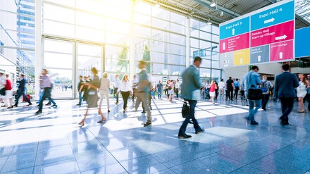 Besucher im Eingangsbereich einer Messe mi großem Richtungsschild