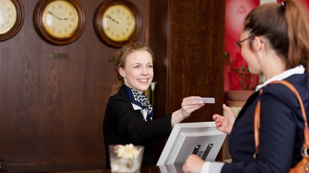 Junge Frau an Rezeption übergibt eine Zimmerkarte an einen weiblichen Gast.