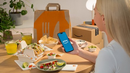 Junge Frau sitzt an einem Tisch mit Essen und einem Handy in der Hand mit der Prime-Website