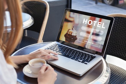 Frau bucht ein Hotelzimmer an ihrem Laptop und trinkt dabei einen Kaffee