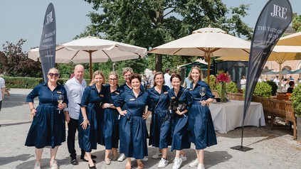 Einige der „starken“ Gastgeberinnen, alle im blauen Kleid zwischen zwei JRE Fahnen
