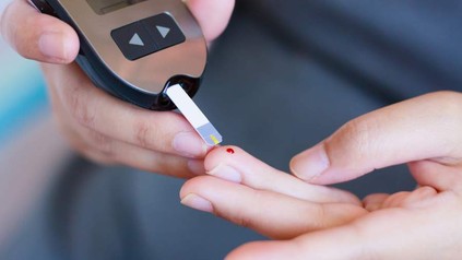 Ein Zuckermessgerät wird an einen leicht blutenden Finger gehalten