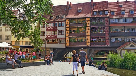 die Krämerbrücke in Erfurt mit Menschen davor an einem sonnigen Tag.
