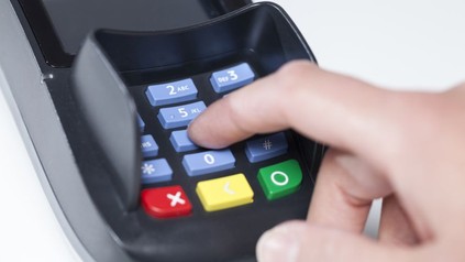 Eine Hand tippt auf einem Kartenzahlgerät eine Geheimzahl ein