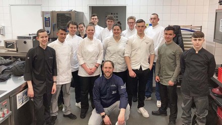 Spitzenkoch Franz Berlin hockt vor einer Gruppe Koch-Auszubildenden in einer Restaurantküche