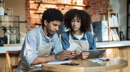 Zwei Gastronomen sitzen am Tisch und schauen traurig auf Papiere