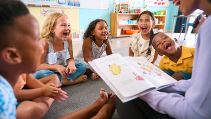 Lachende kleine Kinder, denen ein buch vorgelesen wird