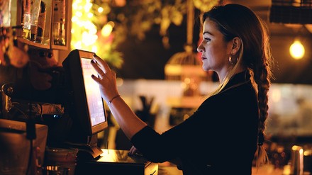 Junge Frau tippt auf einem Touchscreen eines digitalen Kassensystems/Registrierkasse