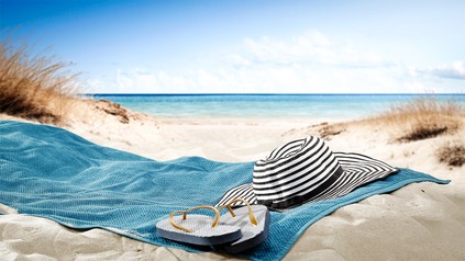 Handtuch, Flip-Flops und Sonnenhut am Sandstrand