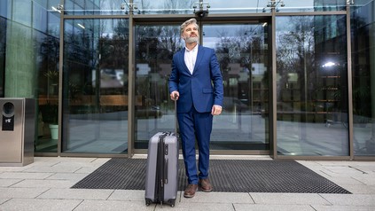 Mann im Anzug und Koffer vor einem Hoteleingang
